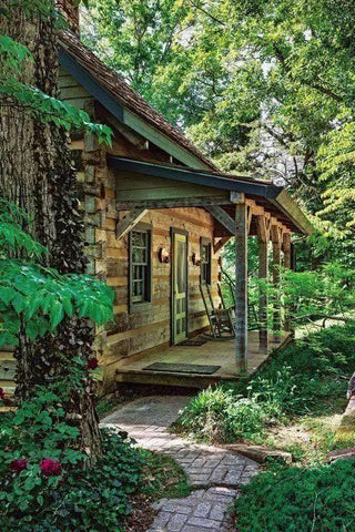 Rustic log cabin with a covered porch surrounded by lush greenery.