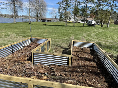 Raised garden beds with metal sides and wooden frames filled with soil and plant debris.