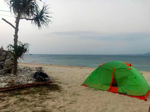 Bright green and red camping tent on a beach with clear blue skies.