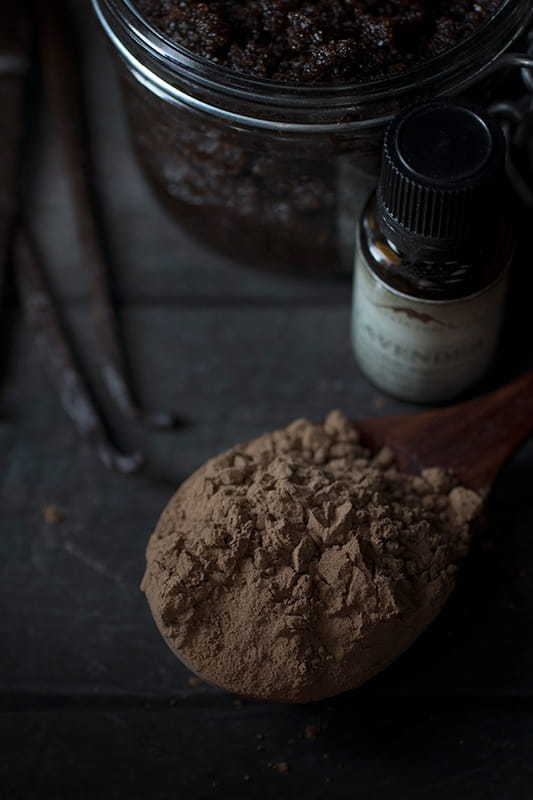 Spoon of roasted cacao powder next to bottle of lavender essential oil as ingredients for Cacao & Vanilla Body Polish Ingredients