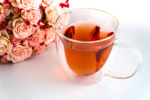 Clear glass cup with amber tea and floating tea leaves in ’The Long History of Tea.