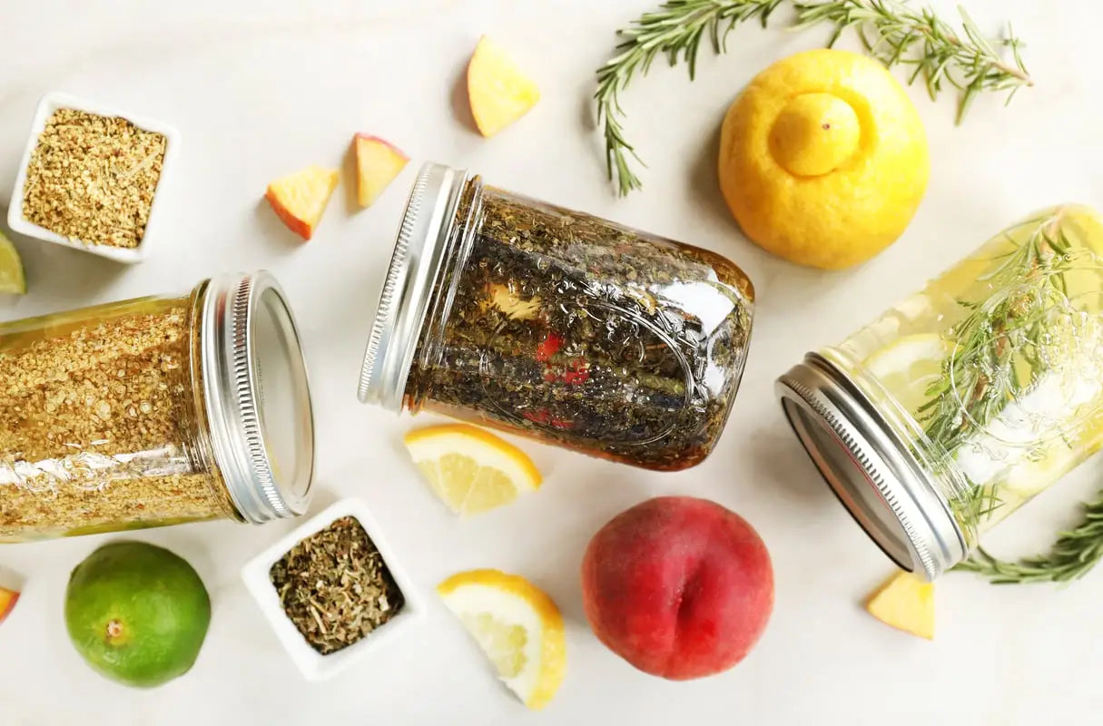 Pint jars  full of ingredients to make herb and fruit infused drinking water, including lemon, balsam, elderflower, peach, and more botanicals.