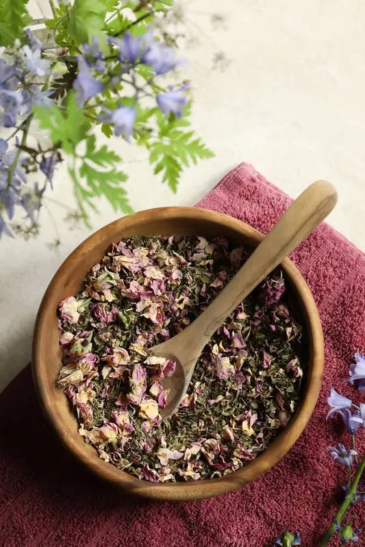 Peppermint, rose, and lemon balm herbal foot soak blend in wooden bowl with spoon.