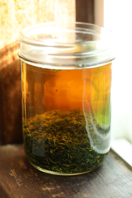 Dried nettle leaves infusing in glass canning jar on windowsill.