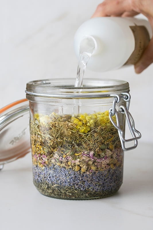 Queen of Hungary's Water dried herbal preparation pantry jar filled with dried herbs and hand pouring extract into jar