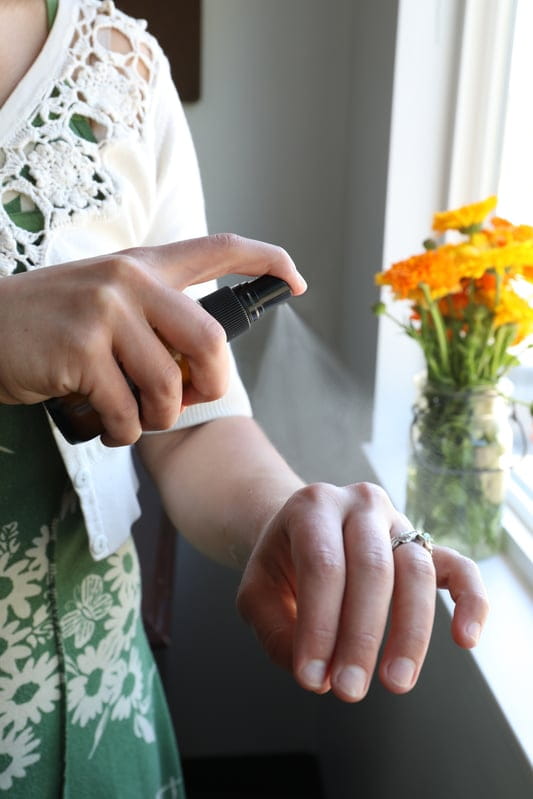 Young woman spritzing liquid on young hand with fresh calendula flowers in window in background. 